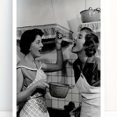 two women in aprons are eating food from the same bowl as they look at each other