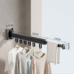 a rack with clothes hanging on it next to a white wall and a black rail