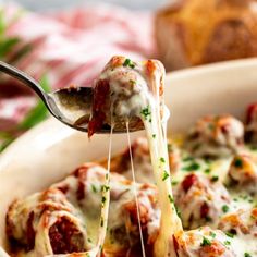 a close up of a plate of food with meatballs and cheese being held by a fork