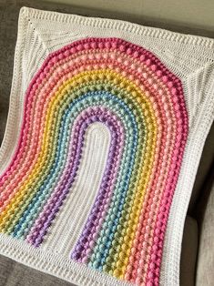 a crocheted blanket with a rainbow design on the front and bottom, sitting on a couch