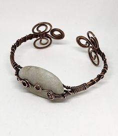 This is a beautiful handmade piece created by Mimi.  This cuff bracelet was made with antique copper 14 gauge and 22 gauge  copper wire.  The stone is an unpolished white beach quartz from Topsail Island NC and is accentuated by two copper swirls. The bracelet is adjustable   About this stone: Some of the NC's beaches have rock pebbles. These Pebbles are derived from older sediment now being reworked in the near shore environment or from offshore rock out-crops on the sea floor. One interesting pebble type consist entirely of quartz that once existed in veins or bands in the original rock....Geologist believe that this gravel like the pebbles are derived from old river beds that once traversed the continental shelf when sea level was lower during ice ages. These deposits now lie beneath th Unique Copper Wire Wrapped Cuff Bracelet, Bohemian Copper Wire Wrapped Cuff Bracelet, Bohemian Hand Forged Copper Cuff Bracelet, Adjustable Wire Wrapped Bronze Cuff Bracelet, Handmade Bohemian Copper Wire Cuff Bracelet, Wire Wrapped Copper Wire Cuff Bracelet Gift, Bronze Wire Wrapped Copper Bracelets, Bohemian Copper Wire Bangle Bracelet, Handmade Copper Wire Cuff Bangle