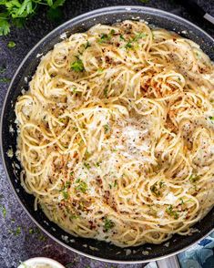 a pan filled with pasta and parmesan cheese on top of a table next to garlic