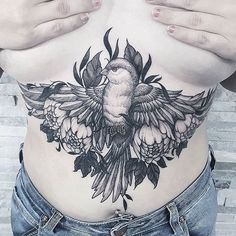 a woman's stomach with a bird and flowers tattoo on her belly, while holding her hands behind her back