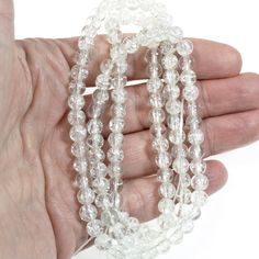 a hand is holding three strands of clear glass beads