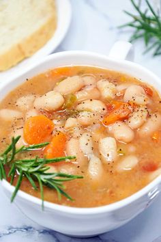 a white bowl filled with beans and carrots on top of a table next to bread