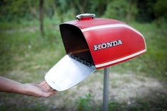 a person holding a metal pan in front of a red and white mailbox with the word honda written on it