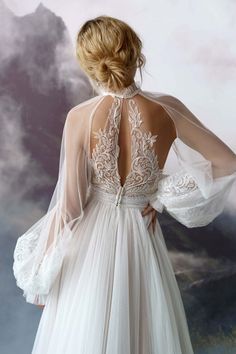 a woman in a white wedding dress with sheer sleeves and an open back, standing against a backdrop of clouds