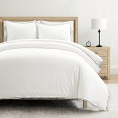 a bed with white sheets and pillows in a room next to a lamp on a table