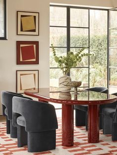 a dining room table with chairs around it and pictures on the wall behind it in front of a large window