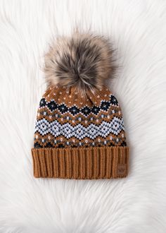 Camel, black, white and blue patterned knit pom hat Cuff detail at the hemline Natural faux fur pom accent Fleece lined Crown patch on the left side One size 100% Acrylic Winter Hat With Pom Poms For Cold Weather, Fall Beanie With Pom Poms For Cold Weather, Winter Hats With Faux Fur Trim, Casual Winter Hat With Faux Fur Trim, Cozy Brown Beanie For Winter, Brown Cozy Winter Beanie, Cozy Brown Winter Beanie, Beanie With Faux Fur Trim For Cold Weather, Cold Weather Beanie With Faux Fur Trim