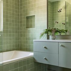 a bathroom with green tiles and a white bathtub next to a sink under a mirror