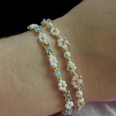 two bracelets with white and blue beads on the wrist, one is gold plated