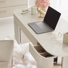 a laptop computer sitting on top of a white desk next to a chair and vase