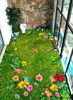 an indoor area with grass and flowers on the ground, next to a window sill