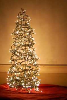 a lit up christmas tree sitting on top of a red cloth covered floor next to a wall