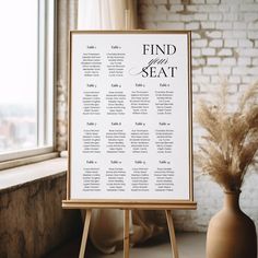 a seating chart on a easel next to a vase with dried grass in it