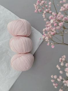 two skeins of pink yarn sitting on top of a white napkin next to flowers