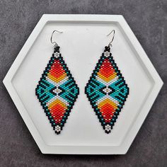 a pair of beaded earrings sitting on top of a white tray next to a hexagonal object