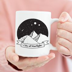 a person holding a coffee mug with the city of starlight on it in their hands