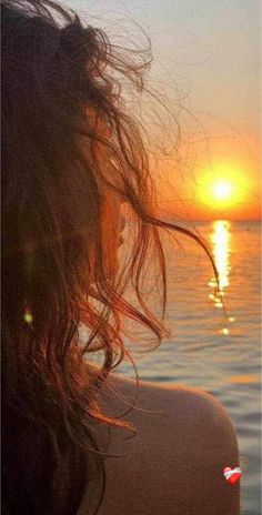 the back of a woman's head as she looks out over water at sunset