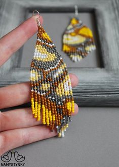 a hand holding a pair of beaded earrings in front of a gray framed frame