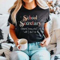 a woman sitting on a couch holding a coffee cup and wearing a school secretary t - shirt