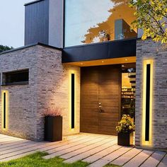 a modern house with brick walls and large glass windows at night, lit up by lights on either side of the entry door