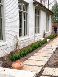 a white brick house with landscaping in the foreground and an orange potted planter on the far side