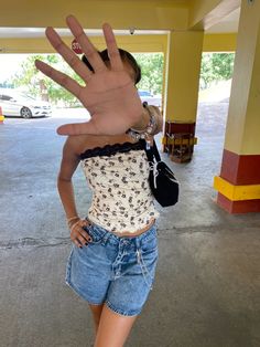 a woman is holding her hand up in front of her face while wearing shorts and a tank top