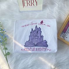 an embroidered book with a castle on it next to some blue flowers and a card that says i'm in my name