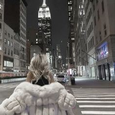 a woman is walking down the street in new york city at night with her fur coat over her shoulders