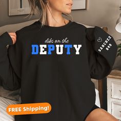 Celebrate the strength and dedication of deputy wives with our Deputy Wife Sweatshirt, a perfect Police Officer Gift. Crafted with comfort in mind, this custom sweatshirt is designed for both him and her, making it an ideal Couples Gift. Show your pride in the Thin Blue Line community with the K9 Police Sweatshirt, a personalized and thoughtful engagement gift for the police officer in your life. Whether it's for Mothers Day or any occasion, this sweatshirt is a stylish and meaningful way to honor the commitment of law enforcement families. About this sweatshirt: - 50% cotton, 50% polyester - Medium-heavy fabric (8.0 oz/yd² (271.25 g/m - Loose fit - Runs true to size - No hood   Sizing details:  - We offer unisex sizing for all tees & sweatshirts. - Our Sweatshirts run about 1 size larger Law Enforcement Family, Deputy Wife, K9 Police, Wife Sweatshirt, Police Shirts, Police K9, Police Officer Gifts, Police Wife, Couples Gift