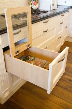 an open drawer in the middle of a kitchen with white cabinets and wood flooring