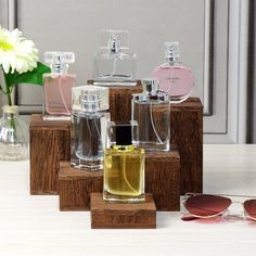 several different types of perfume bottles on wooden blocks with sunglasses and flowers in the background