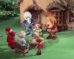 several cartoon characters are standing in front of a small house with thatched roof and grass on the ground