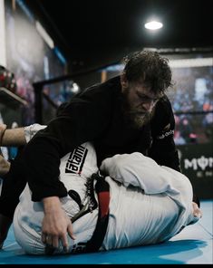 a man in black shirt and white pants on the ground with his hand over another person's leg