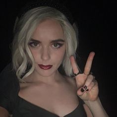 a woman with white hair and black makeup making the peace sign in front of her face