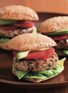 three hamburgers with lettuce, tomato and cheese on a brown plate sitting on a wooden table