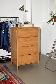 a wooden dresser sitting in front of a rack with clothes hanging on it's hangers