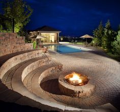 a fire pit in the middle of a brick patio next to a swimming pool at night