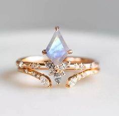 a gold ring with an opal stone and diamond accents on the side, sitting on a white surface