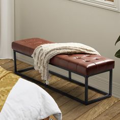 a brown leather bench sitting on top of a hard wood floor next to a bed