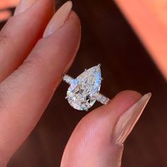 a close up of a person holding a ring with a pear shaped diamond on it