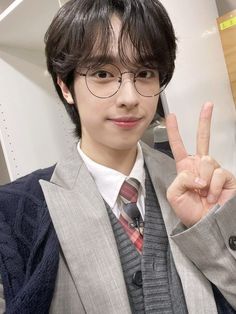 a young man wearing glasses and a suit giving the peace sign with his hand in front of him