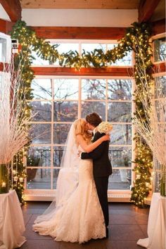 a bride and groom standing in front of an open window at their wedding ceremony with christmas lights on the windows behind them