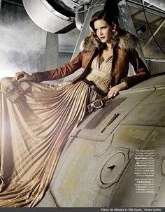 a woman sitting on top of an airplane in front of a jet engine and wearing a fur coat