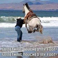 a man is riding a horse on the beach with his feet in the water while another person watches