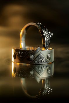 two wedding rings sitting next to each other on top of a reflective surface in the dark