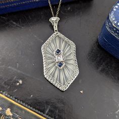 Stunning Art Deco 14K white gold camphor glass pendant. Featuring beautiful filigree work and accented with a small single cut diamond and two calibre cut synthetic sapphires. Camphor glass was designed to simulate rock crystal. This beautiful piece is timeless and elegant. Dimensions:  - pendant measures 46mm x 21mm (including bail) - chain is 17" in length  - weight 6gm Condition: - overall in very good condition with light wear throughout  - few minor marks on glass Art Deco Oval Diamond Necklaces, Art Deco White Gold Necklace With Gemstone, Art Deco White Gold Gemstone Necklace, Art Deco White Gold Necklace With Rose Cut Diamonds, Art Deco Oval Diamond Necklace, White Gold Art Deco Gemstone Necklace, Victorian Blue Jewelry With Diamond Accents, Art Deco Diamond White Necklace For Anniversary, Sapphire And Diamond Accented Platinum Jewelry