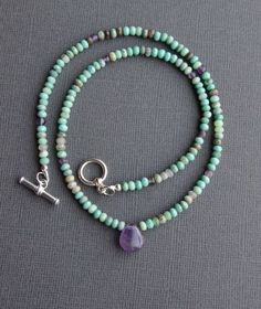 "Chrysoprase and Amethyst Necklace This beaded necklace boasts glorious earthy greens and muted purples, with its combination of chrysoprase and amethyst gemstones. Faceted rondelles of chrysoprase, in all of its natural shades, encircle the neck, sparked with randomly placed amethyst beads. Teardrop amethyst focal pendant. Finished with a sterling silver toggle clasp and findings. Small beads measure about 3.5-4.0mm, and the amethyst drop measures about 11x13mm. Necklace shown measures 18\" in Green Amethyst Gemstone Beads Jewelry, Green Amethyst Jewelry With Gemstone Beads, Bohemian Amethyst Necklace With Gemstone Accents, Bohemian Green Amethyst Jewelry, Bohemian Lavender Hand-strung Jewelry, Turquoise Amethyst Necklace With Natural Stones, Bohemian Purple Necklace With Gemstone Accents, Purple Gemstones, Boho Chic Necklace